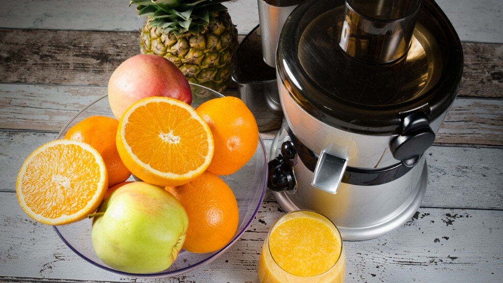 electrodoméstico para extraer zumo de frutas en color gris rodeado de diversos vegetales dentro de una cocina