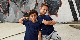 Pareja de 2 niños pequeños, ambos con playera azul, manga corta, el de la derecha flexiona el brazo derecho en pose de fuerza, y el de la izquierda tiene los brazos cruzados al altura del pecho, en pose de fuerza.